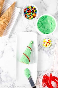 a white plate topped with green frosting next to bowls of candy and an ice cream cone