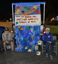 two people sitting in front of a truck decorated with lights and fish on the side