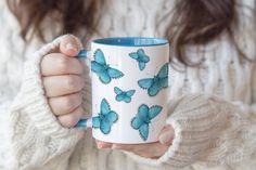 a woman is holding a coffee mug with blue butterflies on it and she has her hands in the cup