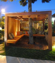 a wooden gazebo sitting on top of a lush green field next to a tree