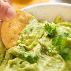 a person dipping guacamole into a bowl with tortilla chips on the side