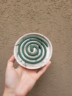 a hand holding a white and green plate with spiral design on it's side