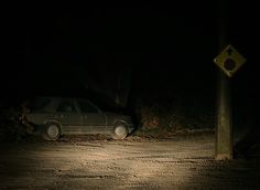 a car is parked in the dark on a dirt road near a street sign and traffic light