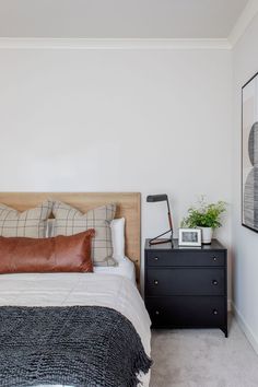 a bed sitting next to a nightstand with a lamp on top of it and a black dresser