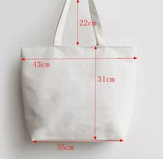 a white canvas tote bag with measurements for the size and width, hanging on a wall