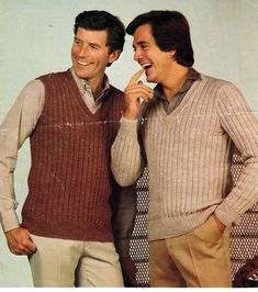 two men standing next to each other smiling and talking on cell phones while wearing sweater vests