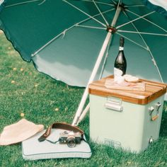 an open umbrella sitting next to a cooler on the grass