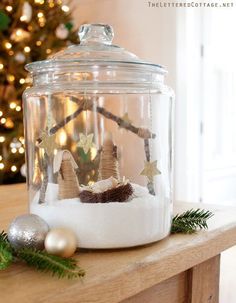 a christmas scene in a glass jar with snow on the ground and ornaments around it