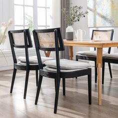 a dining room table with chairs and a vase on the side, in front of a window