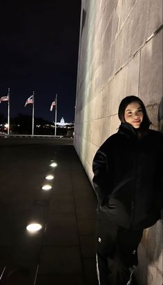 a woman standing next to a wall at night