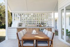 a wooden table sitting under a white pergoline covered outdoor kitchen with an oven