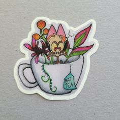 a sticker with an image of a cat in a coffee cup filled with flowers