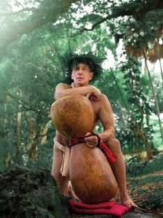 a man sitting on top of a rock in the forest holding a large piece of wood