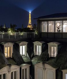 the eiffel tower is lit up at night from across the roofs of buildings