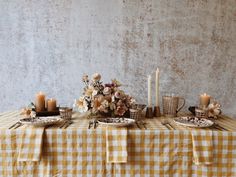 a table topped with plates and candles next to a vase filled with flowers on top of a checkered table cloth