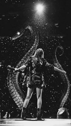 a woman standing on top of a stage with her arms out in front of an enormous snake