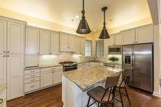 a kitchen with an island and two pendant lights over the stove top, refrigerator and microwave