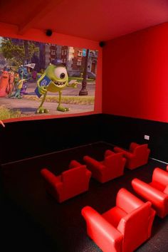 an empty movie theater with red seats and cartoon characters on the screen in front of them