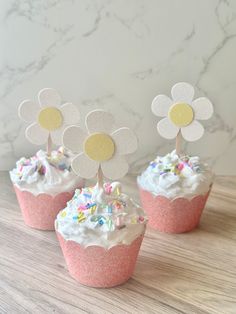 three cupcakes with white frosting and sprinkles decorated with flowers