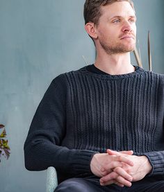 a man sitting in a chair with his hands folded and looking off to the side