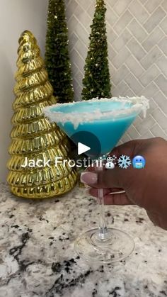 a person holding a martini glass in front of a christmas tree with snow flakes on it