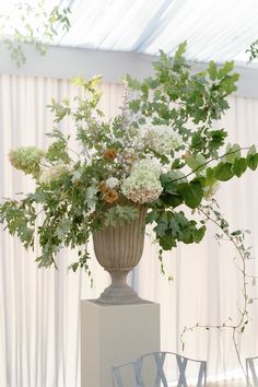 a vase filled with lots of flowers sitting on top of a white pedestal next to chairs