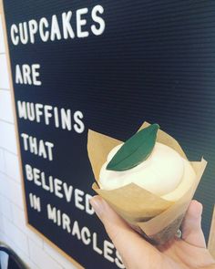 a person holding up a cupcake in front of a sign