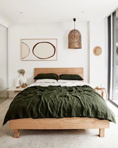 a bed with green sheets and pillows in a bedroom next to a large window that looks out onto the outdoors