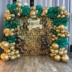 a large green and gold balloon arch in front of a white wall with balloons on it