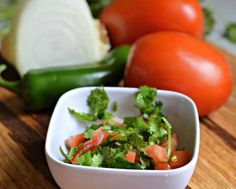 some tomatoes and lettuce in a white bowl on a wooden table next to other vegetables