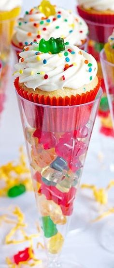 four cupcakes with white frosting and sprinkles on them sitting in small cones