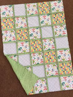 a green and white quilted blanket on top of a brown floor next to a piece of cloth