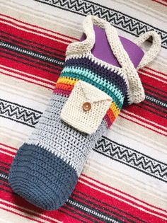 a crocheted bag with a button on it laying on a striped rug next to a purple object