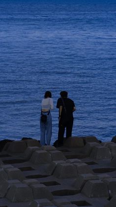 two people are standing on the rocks by the water