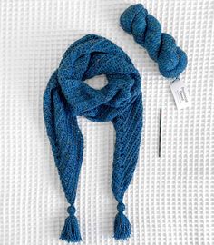 a blue knitted scarf next to a skein of yarn and a knitting needle