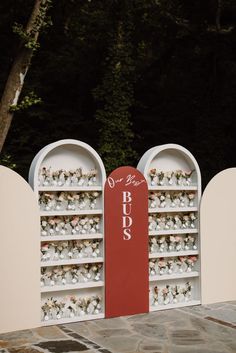 a red and white display case filled with lots of small vases next to trees