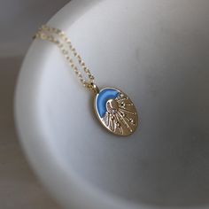 Light up your style with our Gold Filled Crescent Moon & Stars Oval Charm Necklace, a celestial-inspired piece that brings the magic of the night sky into your everyday wardrobe. This enchanting necklace features an oval-shaped charm with a serene blue background, adorned with a delicate crescent moon at its center. The moon is surrounded by bursts of light leading to tiny stars, all accented with sparkling cubic zirconia stones that add a touch of brilliance to the design.  This celestial neckl Blue Sun And Moon Pendant Necklace, Blue Celestial Necklaces With Sun And Moon Design, Blue Necklace With Sun And Moon Design For Gift, Blue Sun And Moon Necklace For Gift, Blue Sun And Moon Design Necklace For Gift, Blue Celestial Necklace With Moon Charm, Celestial Pendant, Celestial Necklace, Tiny Star