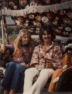 an old photo of two people sitting next to each other in front of a floral wall