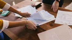 three people sitting at a table with papers on top of it and one person holding a pen