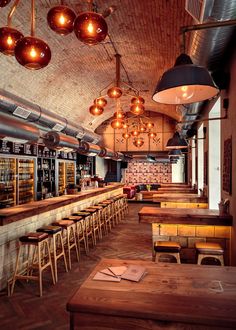 an empty restaurant with wooden tables and stools in front of the bar lights hanging from the ceiling