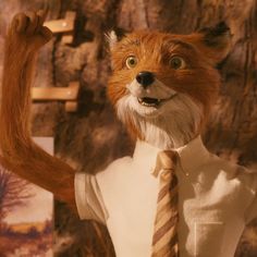 a fox dressed in a shirt and tie with his hands up to the side while standing next to a tree