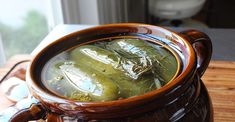 a brown pot filled with green liquid sitting on top of a wooden table next to a window