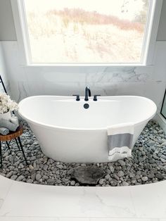 a white bath tub sitting under a window next to a wooden chair and flower pot