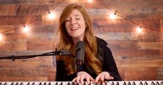 a woman with long red hair is playing the piano and singing into a microphone in front of a wooden wall