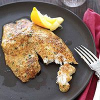 some food is on a black plate with silverware and lemon wedges next to it