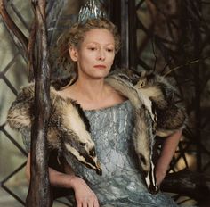 a woman sitting in a chair with two raccoons on her shoulders and wearing a tiara