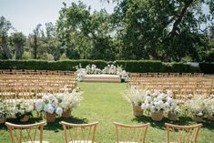 an outdoor ceremony setup with white flowers and greenery on the lawn, surrounded by wooden chairs