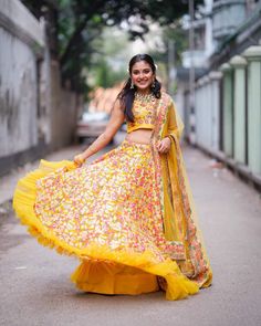 a woman in a yellow and pink lehenga is standing on the street with her arms around her waist