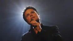 a man holding a microphone in his right hand and singing into the microphone on stage