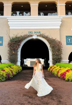 a woman is walking in front of the del mar hotel and resort entrance with flowers all around her